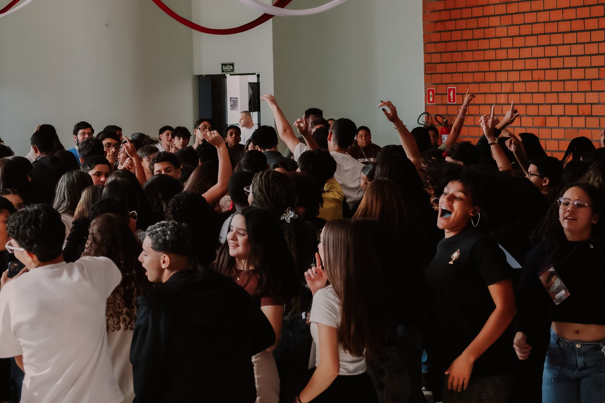 Jovens com os braços erguidos, cantando e pulando juntos num salão durante o Retiro Maranata